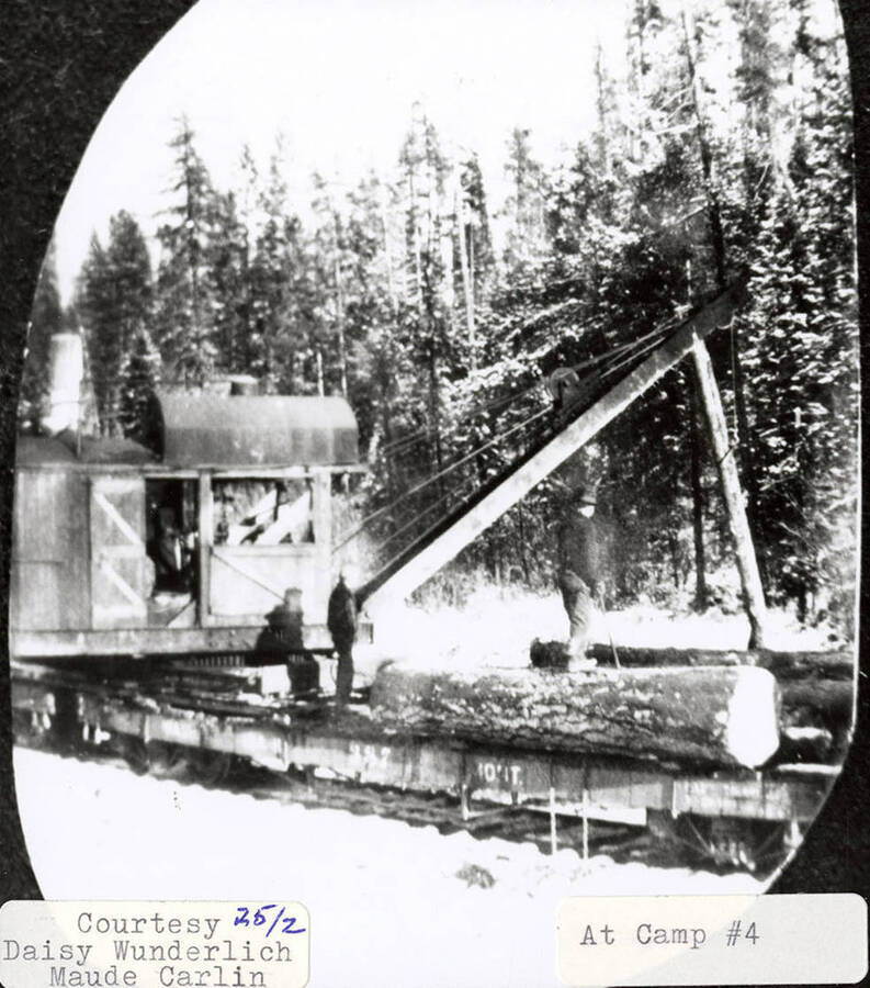 View of the logging equipment at Potlatch Lumber Company Camp #4. A few men can be seen standing on logs sitting next to the equipment.