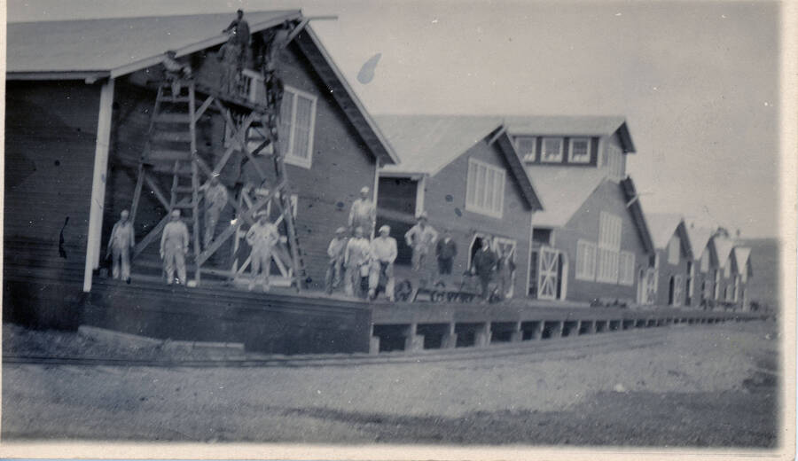 Some of the first stores in Potlatch, Idaho. Workers pose on the boardwalk and on scaffolding next to the buildings.