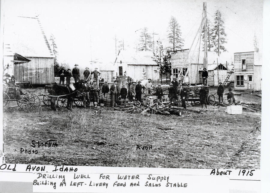 A group of men are gathered to drill a well for water supply at Old Avon, Idaho. The building on the left is the livery feed and sales stable.