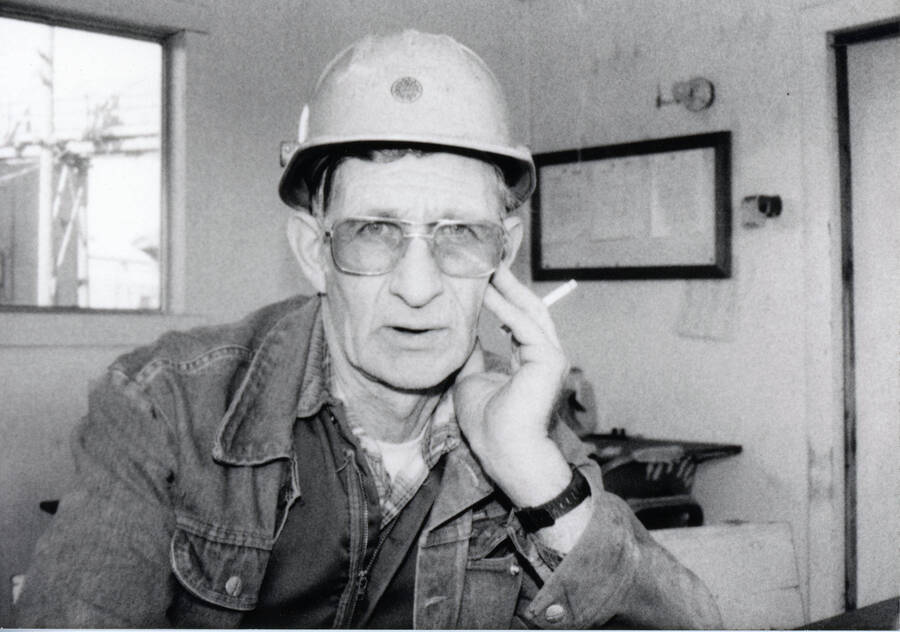 Glen Fuchs poses for a photograph while wearing a hardhat, cigarette in hand.
