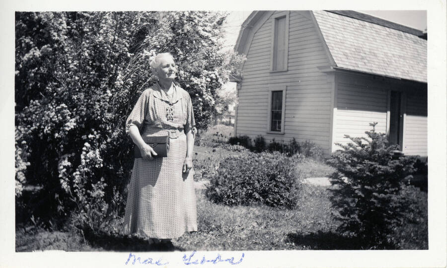 May Gibbs stands in front of a house.