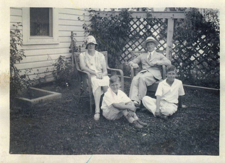 Photograph of William E. "Chappie" Hearn (in chair at right) and his family in front of their house. Pearl is seated in the chair on the left and their sons Rodney (left) and Phillip are seated in front of them on the ground.