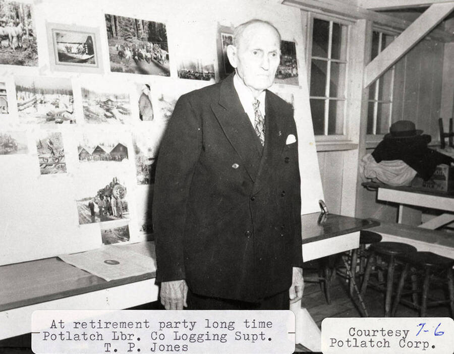 T. P. Jones, the long time Potlatch Lumber Company superintendent, at a retirement party. He is standing in front of a board that has a bunch of pictures on it.
