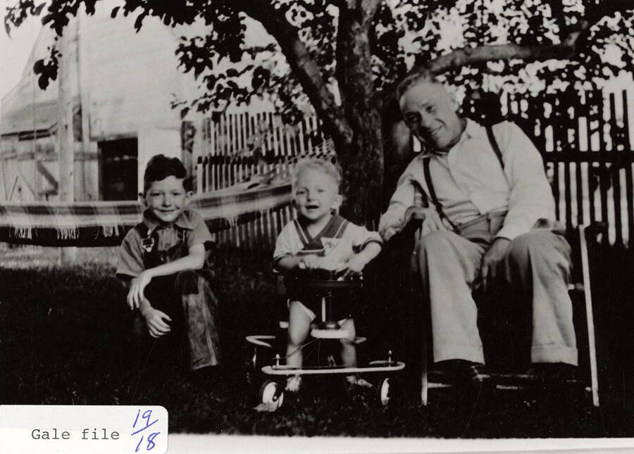 Rev. Dick Ferrell sitting with two boys, Lee Jr. and David (in stroller), in a yard. A hammock can be seen hanging from a tree in the background.