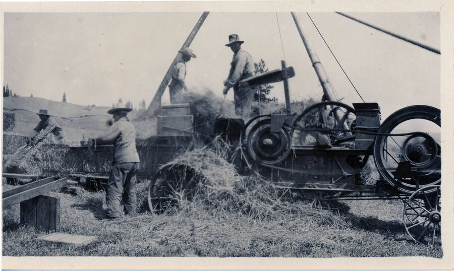 A group of men uses early farming machinery to bale hay at the Bysegger place.