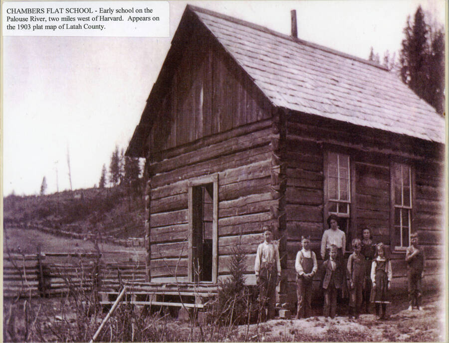 Chambers Flat School. A student stands on the front porch, while another pokes their head out of the schoolhouse door. George Cochrane's property is visible in the background on the left, while Frank Cochrane's property is visible to the right.
