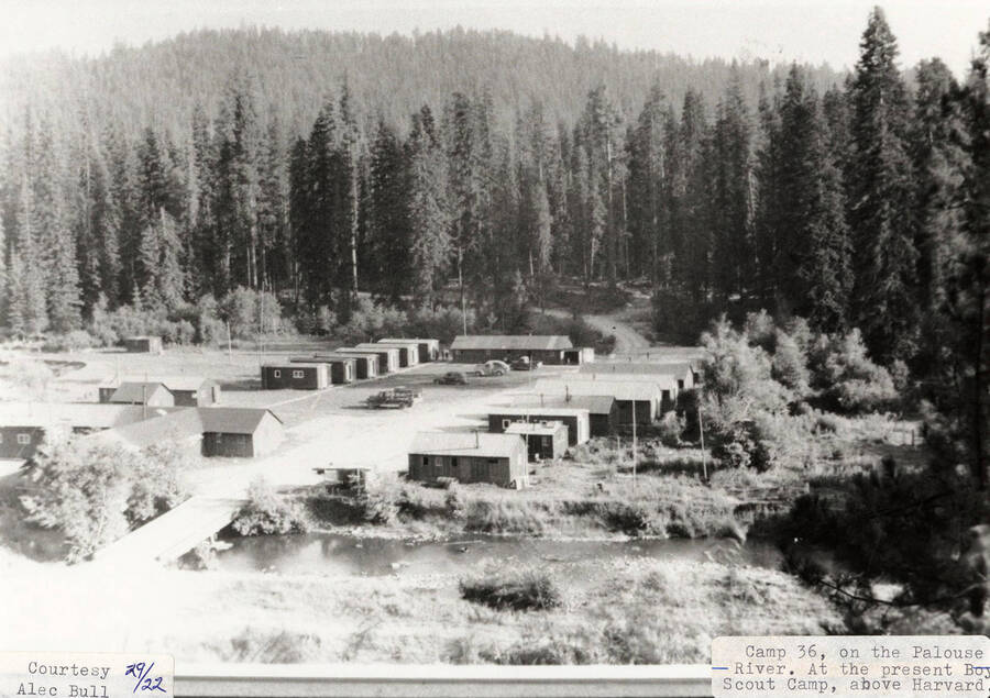 View of PLC Camp 36, which is located on the Palouse River above Harvard, Idaho. Buildings can be seen on the camp, along with a few cars parked in the middle. The camp is presently a Boy Scout Camp.