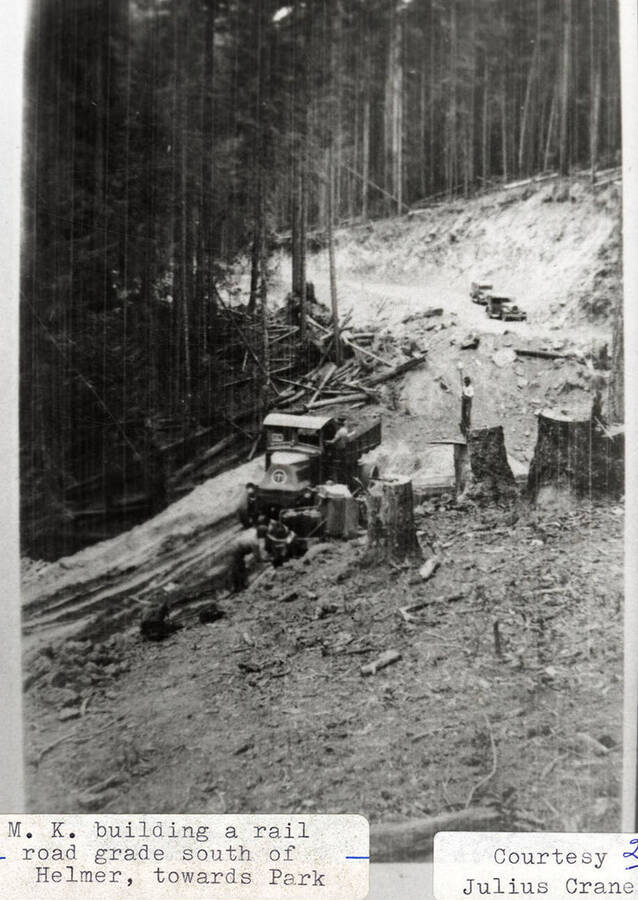 M. K. building a railroad grade south of Helmer, towards Park. A man can be seen standing on a truck as it drives down the road.