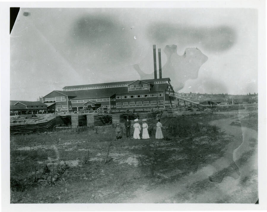 Photograph of three women standing in front of the Potlatch Mill.