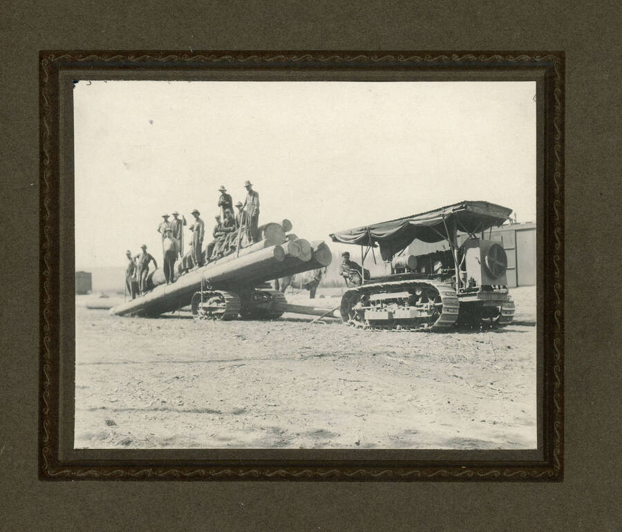 Men standing on logs with cat and trailer.