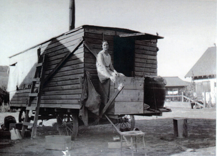 Photograph of Leona Carscallen sitting in front of the cookhouse during harvest.