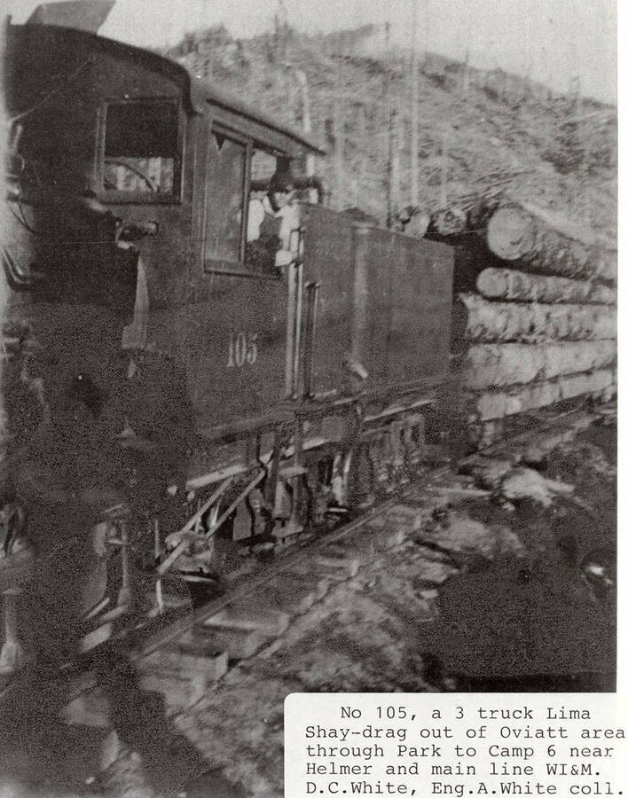 View of a No. 105 locomotive hauling stacks of logs to Camp 6, which is located near Helmer, Idaho and the WI&M main line. A man can be seen in the window of the locomotive.