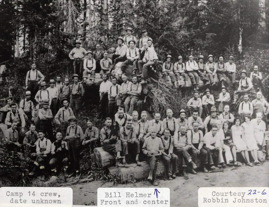 Group photo of the crew of Camp 14. Most the men can be seen wearing suspenders and hats and a few women can be seen sitting in the front row. Bill Helmer is sitting in the front row on the far left.