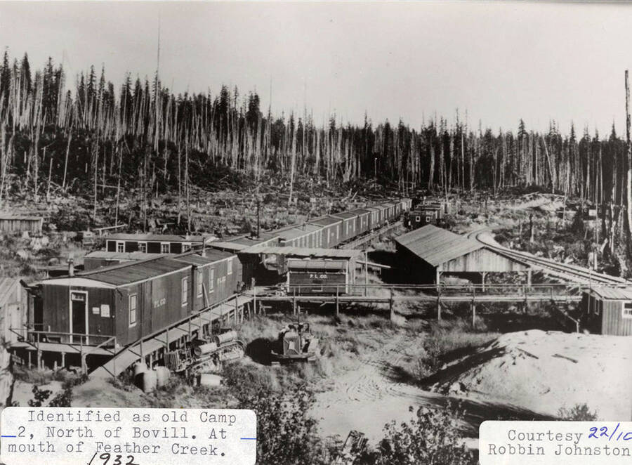 View of old Camp 2, which is located north of Bovill, at the mouth of Feather Creek. Buildings can be seen sitting on stilts and a railroad can be seen running on the right side of the camp.
