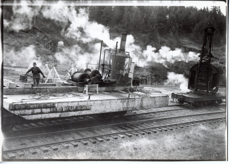 Photograph of a steam donkey on a flat car by the Rock Creek Bridge.
