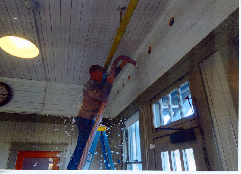 Photograph of man blowing insulation into the walls on the first floor of the WI&M Depot.
