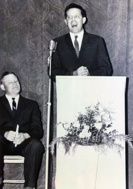 Photograph of Senator Frank Church delivering graduation address with Dwight Strong looking on.