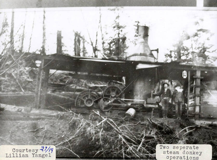 View of two steam donkey operations. Two men can be seen standing next to the equipment.