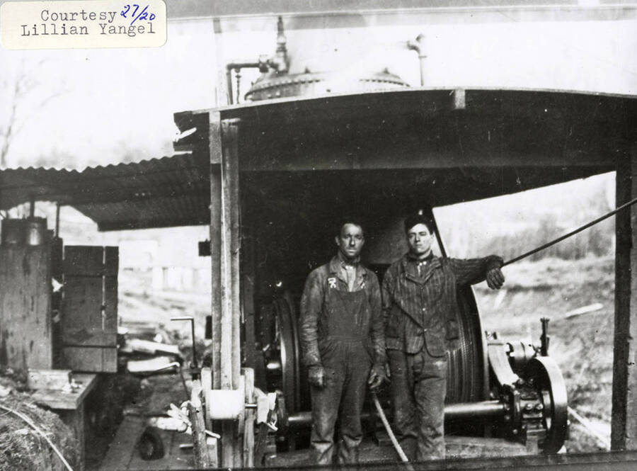 Two men standing in front of a steam donkey engine.