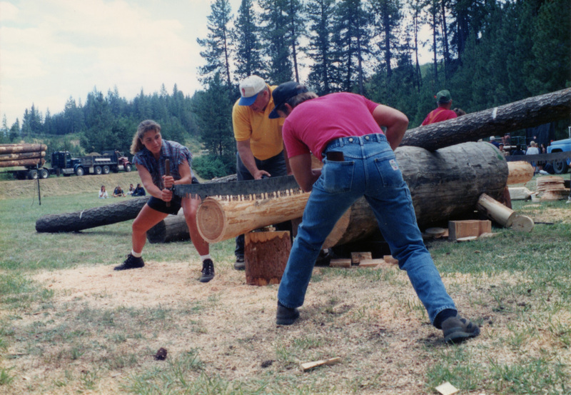 Photograph of Edie Walser, Aaron Walser, and Richard Falk cutting a log at Potlatch Days.