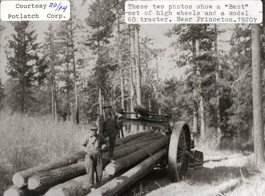 View of a 'Best' set of high wheels and a model 60 tractor. Two men can be seen standing on top of a stack of logs that are chained to the tractor.