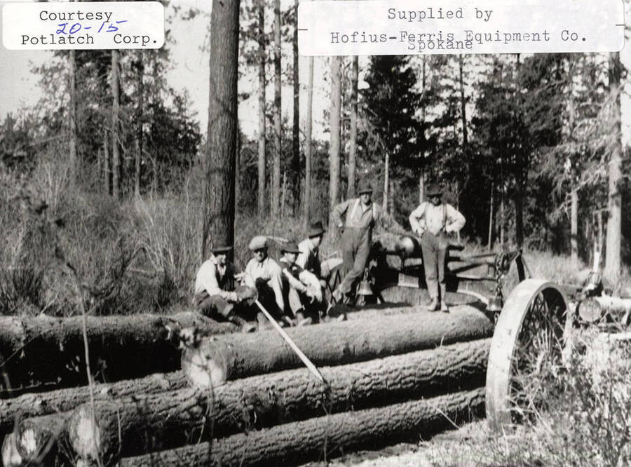 View of a 'Best' set of high wheels and a model 60 tractor. A group of men can be seen standing on top of a stack of logs that are chained to the tractor.