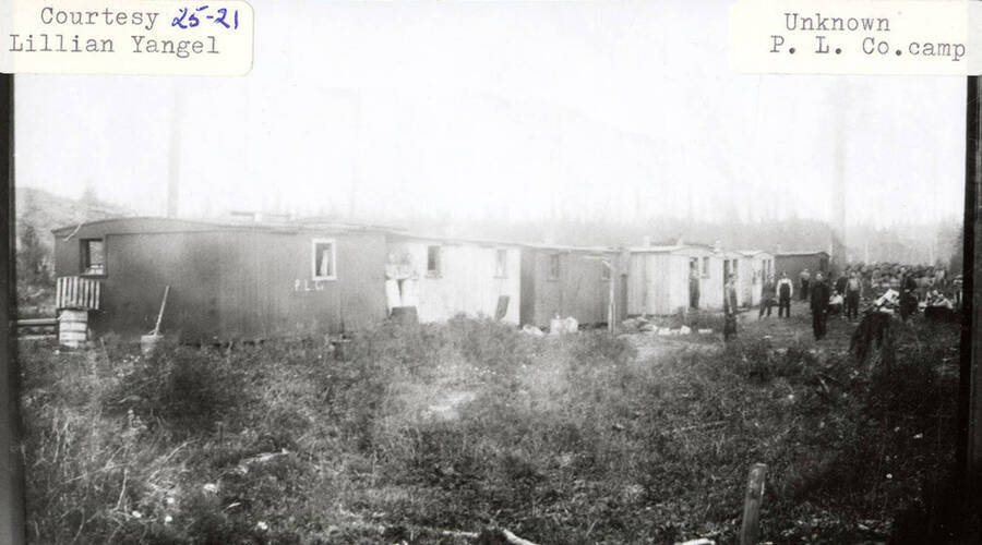 View of a Potlatch Lumber Company camp. Men can be seen standing next to buildings in the camp.
