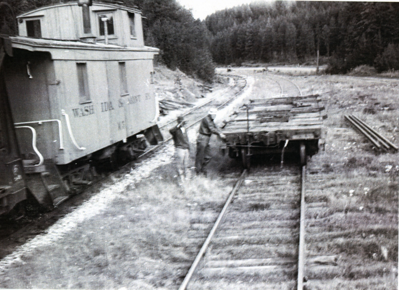 Photograph of a brakeman with Caboose X-5 and a flat car on a siding at the WI&M Railway Depot in Potlatch.