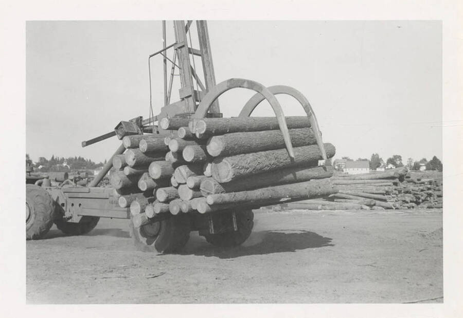 A closer side view of the LeTourneau log unloading machine with grappling-like hooks carrying a bundle of logs.