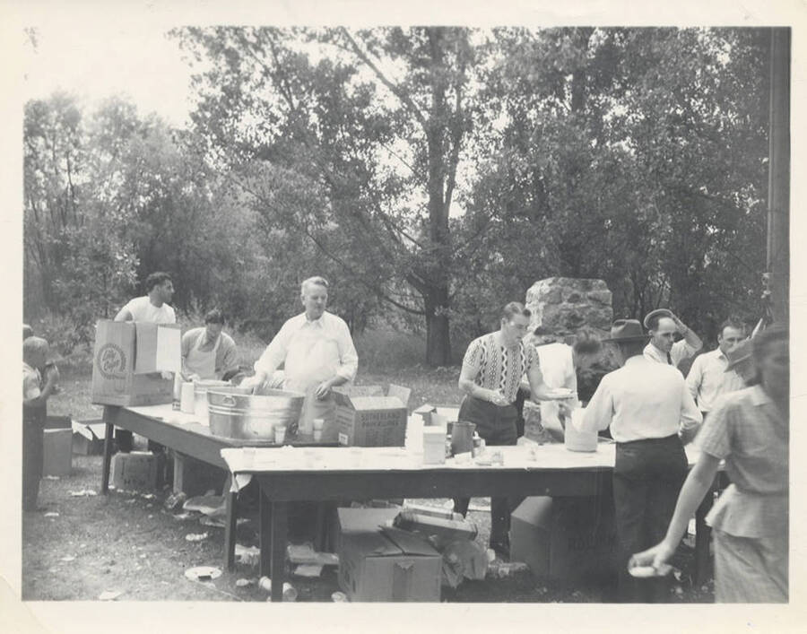 A group of people behind tables with boxes of cups and paper ware.