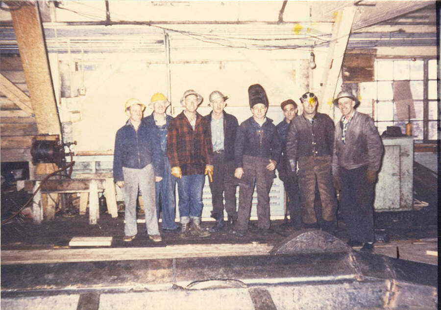 A group of eight men in a building wearing hats.