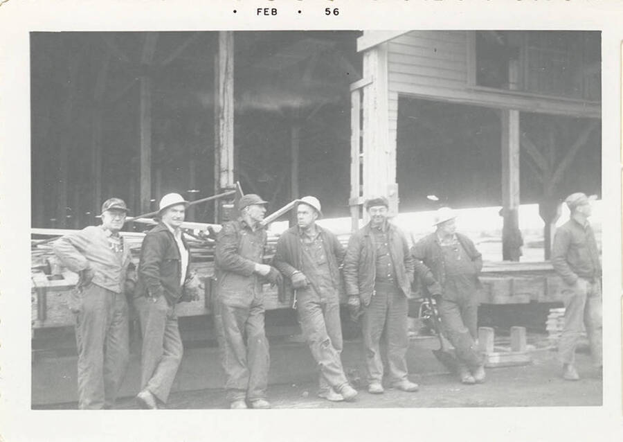 A photograph of seven men. Some are posing, some are conversing, and some are walking away.