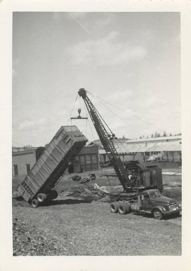 A crane lifting a large container that appears to attach to trucks.