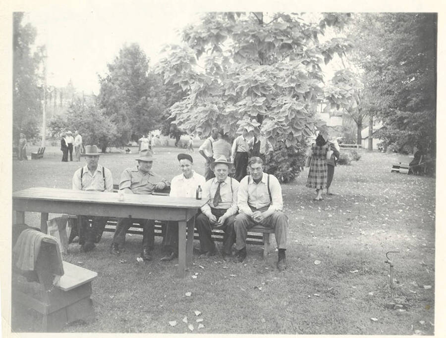 A photo of five men on a bench at a park for some type of gathering.