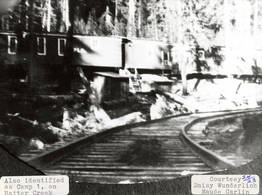 View of a railroad track running through Camp 1, which is located on Hatter Creek. A few railroad cars can be seen behind the tracks.