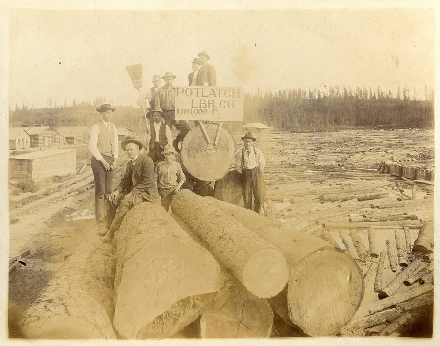 Employees on a stack of logs by the log pond holding a sign that reads 'Potlatch LBR.CO. 1,110,000 Ft.'