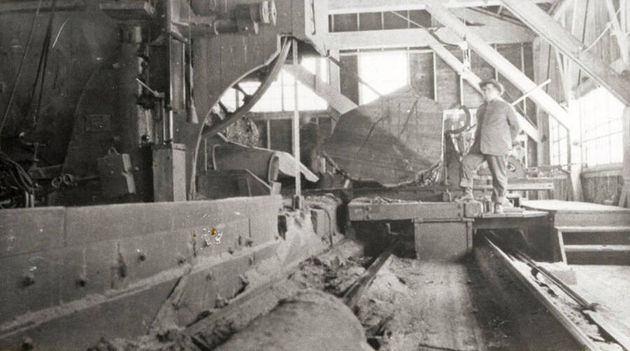 A photograph of a single employee next to a large machine and log at the lumber mill.