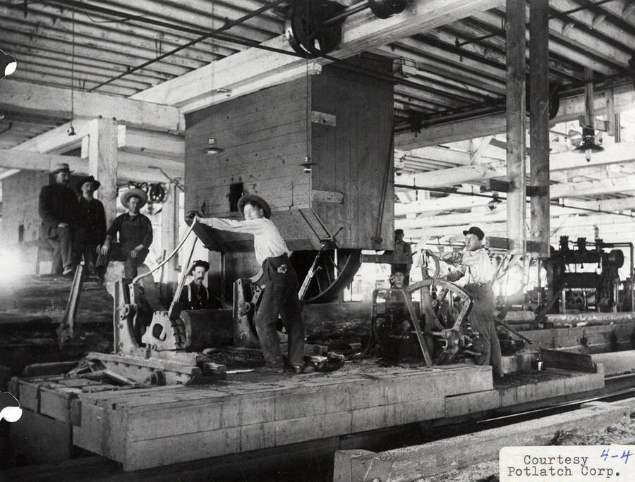 A photograph of employees in Potlatch, ID with a machine to debark lumber.