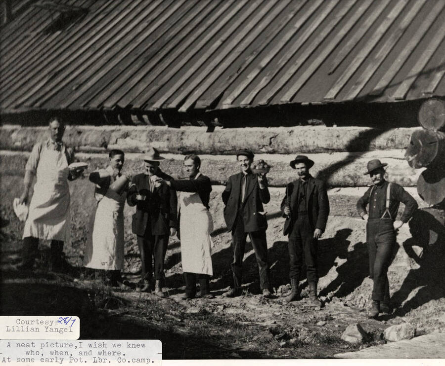 A group of men holding food and drinks outside a log cabin at a PLC camp.