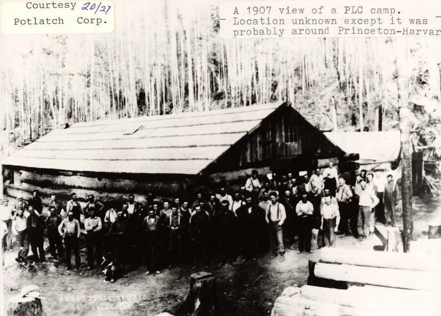 View of a group of people standing outside a log cabin at a PLC camp, located around Princeton-Harvard, Idaho.