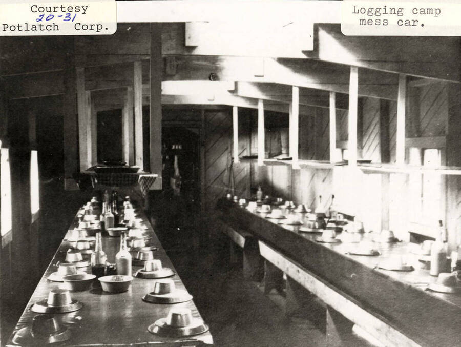View of the mess car at a logging camp. The tables can be seen set with dishes.