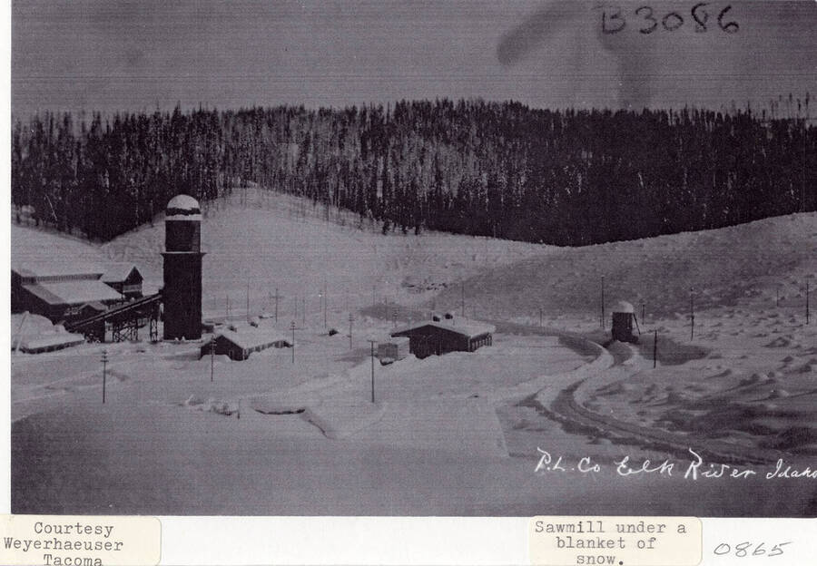A photograph of the Potlatch Lumber Company's sawmill in Elk River, Idaho under a blanket of snow.