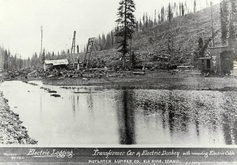 A photograph of a transformer car and electric donkey with a connecting electrick cable at the Potlatch Lumber Company Elk River, Idaho Camp.Used for electric logging with E.J. Barry as the electrical engineer.