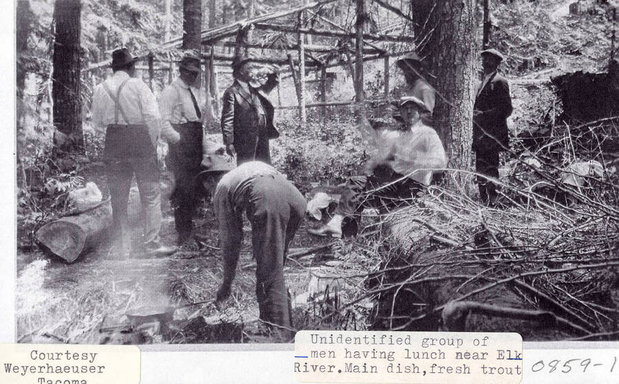 A photograph of unidentified men eating fresh trout for lunch near Elk River.