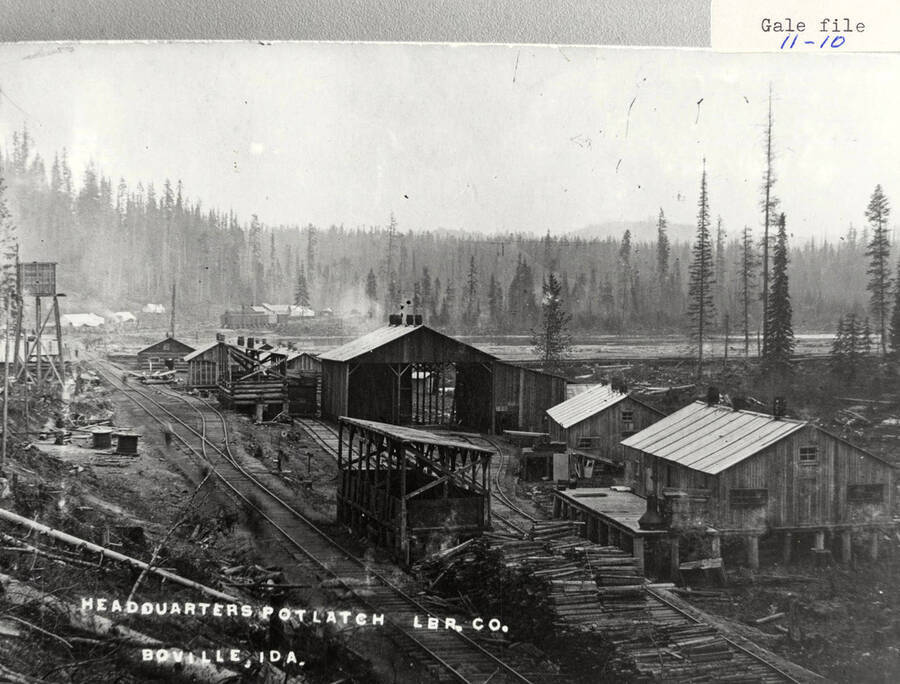 View of PLC headquarters, located in Bovill, Idaho. Log cabins and log piles can be seen scattered around the camp. A railroad runs through the camp.