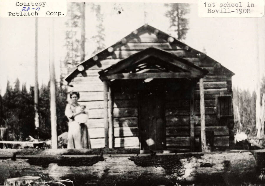 View of the first school in Bovill, Idaho. A woman can be seen standing outside of the school.