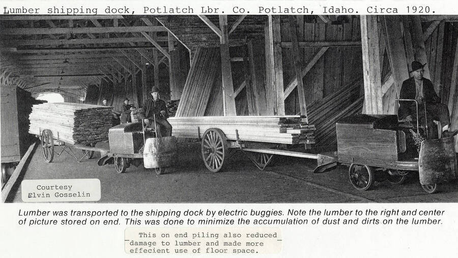 A photograph of the lumber shipping dock at the Potlatch Lumber Company in Potlatch, Idaho around 1920. The workers are on electric buggies to transport lumber to the shipping dock. The lumber is stacked on end in the back to prevent dust accumulation, reduce lumber damage, and efficiently use floor space.