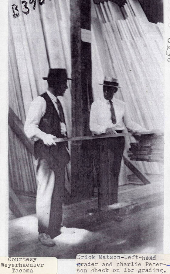 A photograph of Erick Matson and Charlie Peterson checking on lumber grading.