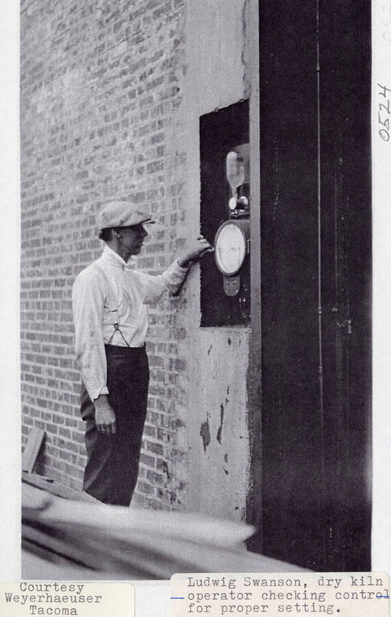 A photograph of the dry kiln operator Ludwig Swanson checking control for proper settings.