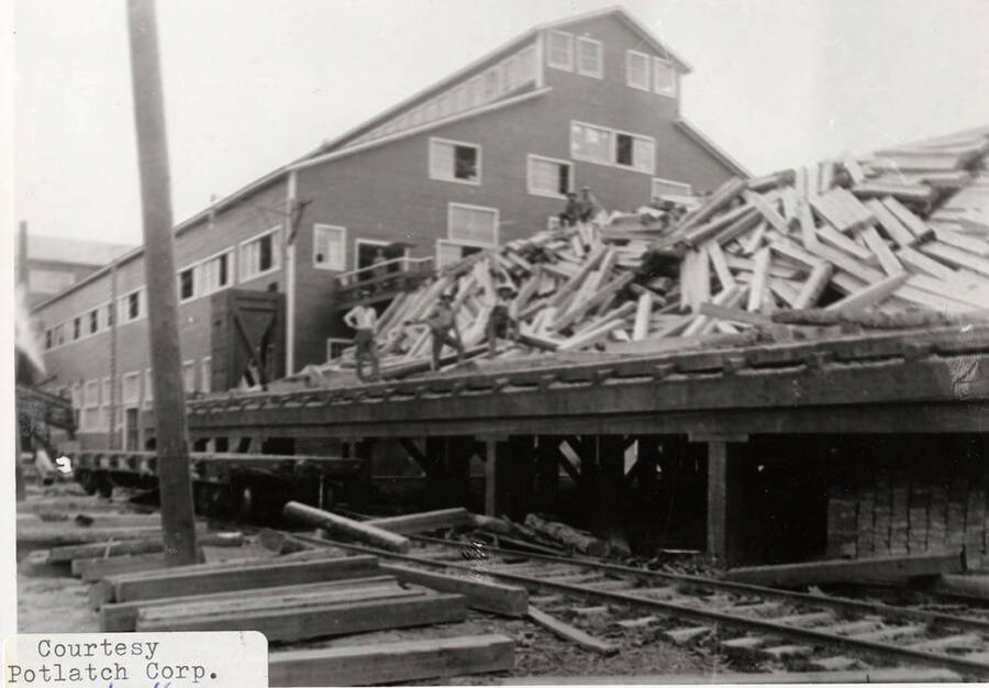 A photograph of a large pile of lumber on the shipping dock.